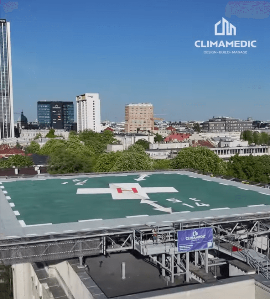 Lądowisko dla helikopterów na dachu budynku szpitala w mieście, z logo firmy Climamedic na banerze i w prawym górnym rogu.